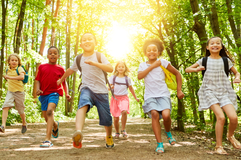 Image of 6 kids in the forest wearing backpacks running toward the camera
