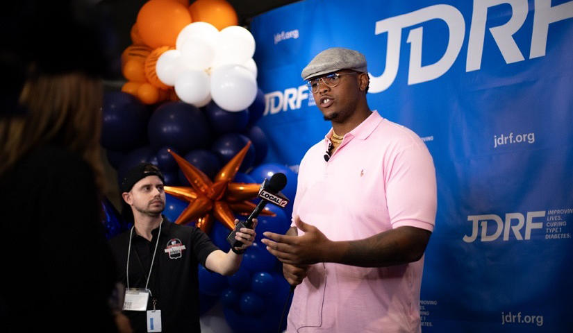 Orlando Brown, Jr. speaks to reporters in front of a blue JDRF backdrop with orange and white ballons