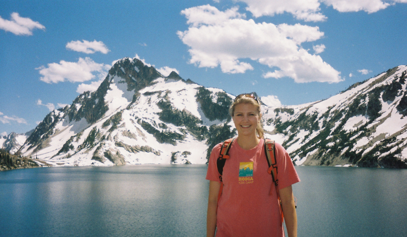 Lisa Gier in the foreground wearing a Camp Hodia shirt with a lake and snow-capped mountain in the background