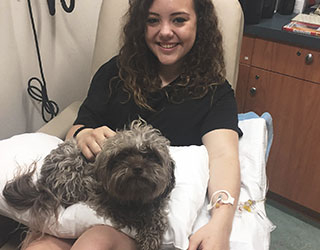 A smiling girl having blood drawn with her dog on her lap